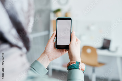 Close up of ethnic young woman holding smartphone in office focus on blank white screen, copy space