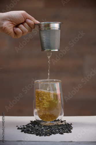Hand pouring hot tea through strainer into glass cup