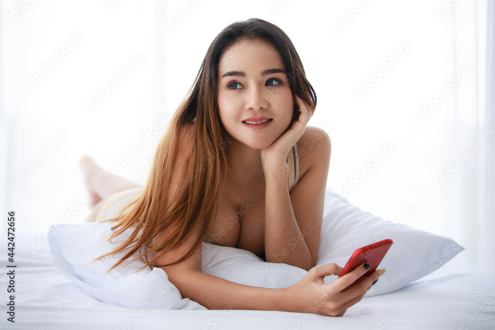 Young Asian woman with smartphone resting on bed Young Asian woman with smartphone resting on bed