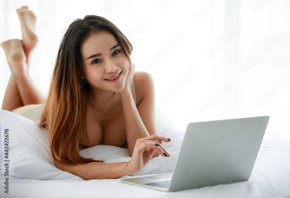 Young Asian female resting on bed and using netbook Young Asian female resting on bed and using netbook