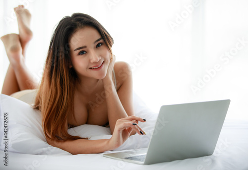 Young Asian female resting on bed and using netbook