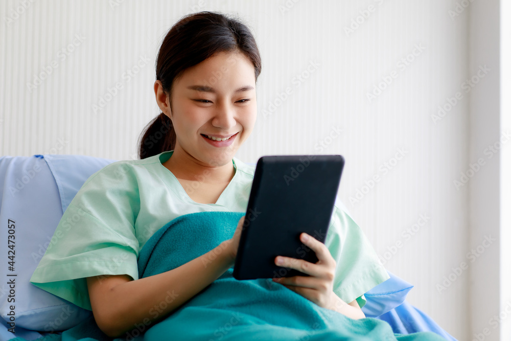 An asian young pretty female patient smiling with happiness and touching screen of tablet for online chat or communicate while lying on bed in hospital. Technology and Medical Concept. An asian young pretty female patient smiling with happiness and touching screen of tablet for online chat or communicate while lying on bed in hospital. Technology and Medical Concept.