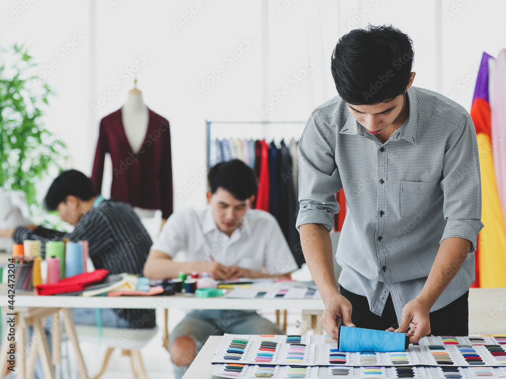 Asian tailor cutting fabric near colleagues Asian tailor cutting fabric near colleagues