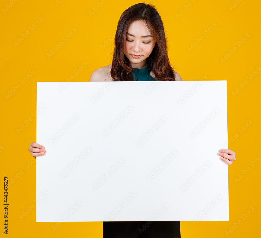 Cute and pretty curly hair Asian female brunette holding white blank board poses to camera with a joyful for advertising and banner use purpose, studio shot isolated on bright yellow background Cute and pretty curly hair Asian female brunette holding white blank board poses to camera with a joyful for advertising and banner use purpose, studio shot isolated on bright yellow background