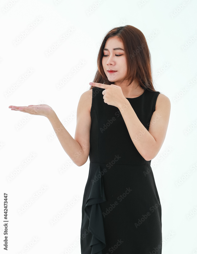 A beautiful young smart businesswoman wearing black dress standing on white background, holding something on the palm of her right hand and pointing finger to present a product or text on copyspace A beautiful young smart businesswoman wearing black dress standing on white background, holding something on the palm of her right hand and pointing finger to present a product or text on copyspace