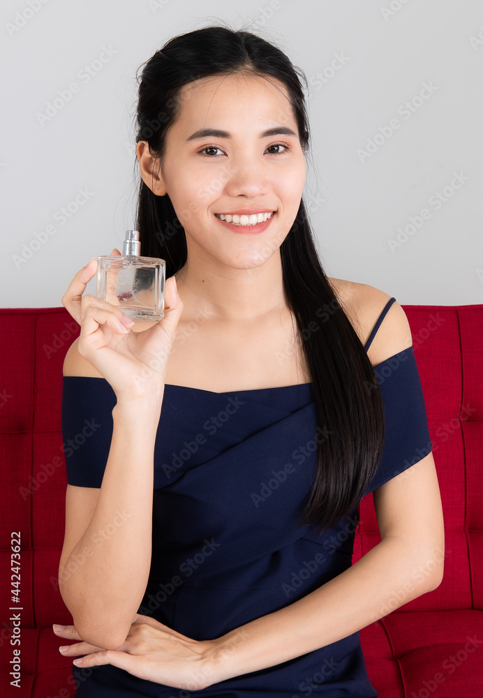 Image of portrait. Smiling Asian woman sitting on Red sofa model is showing of perfume.in the white room at the studio. Concept Product camera picture studio. Image of portrait. Smiling Asian woman sitting on Red sofa model is showing of perfume.in the white room at the studio. Concept Product camera picture studio.