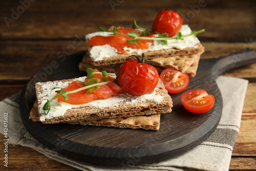 Fresh rye crispbreads with salmon, cream cheese and tomatoes on wooden table, closeup