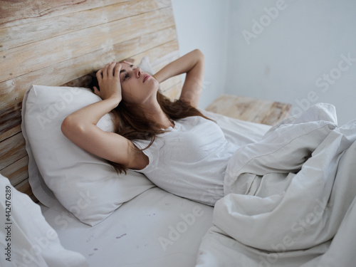woman holding her head with her hands while lying in bed upset feeling unwell