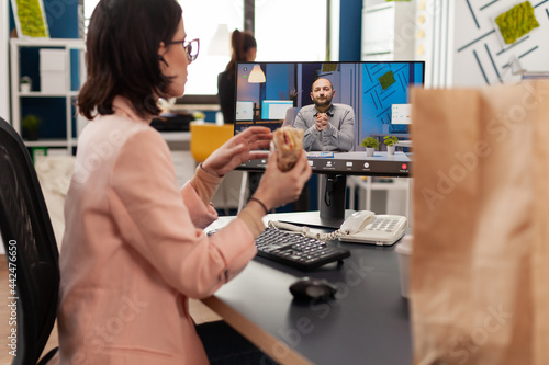 Fotografi Businesswoman eating delivery takeaway sandwich during online videocall conference meeting discussing with remote coworker
