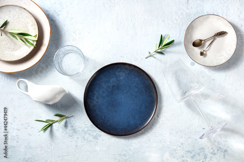 Modern tableware, overhead flat lay shot with a blue plate and olive branches. Mediterranean cuisine restaurant concept. Trendy dishes and glasses, shot from above