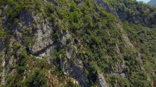 Aerial shot sport fpv drone flying over high cliff mountain covered by dense green trees Abkhazia, Yupsharsky canyon. Amazing natural rock under clear blue sky surrounded by valley scenery landscape photo