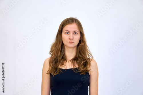 The woman thought for a moment and looks with surprise. A beautiful Caucasian woman stands on a white background in a blue sweater with loose hair. The woman shows emotions.