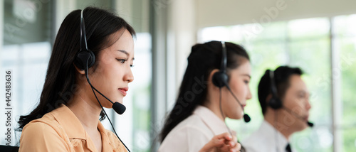 Team of call center staff in Asia wears headphones with a microphone. Smile while serving customers at desks and computers. Service concept and consulting. Communication concept.