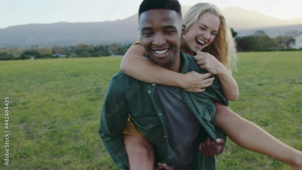 Mixed race romantic couple enjoying time together bonding while giving piggy pack rides in park Mixed race romantic couple enjoying time together bonding while giving piggy pack rides in park