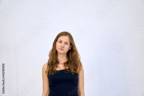 A beautiful Caucasian woman stands on a white background in a blue sweater with loose hair. The woman shows emotions.