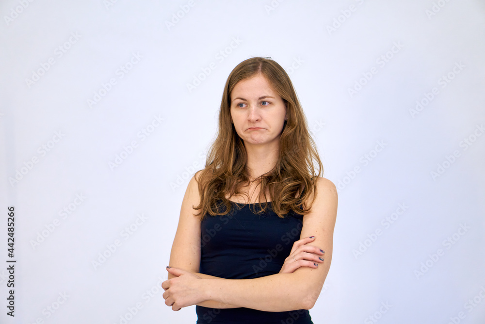 A sad woman stands with her arms crossed over her chest. beautiful Caucasian woman stands on a white background in a blue sweater with loose hair. The woman shows emotions. A sad woman stands with her arms crossed over her chest. beautiful Caucasian woman stands on a white background in a blue sweater with loose hair. The woman shows emotions.