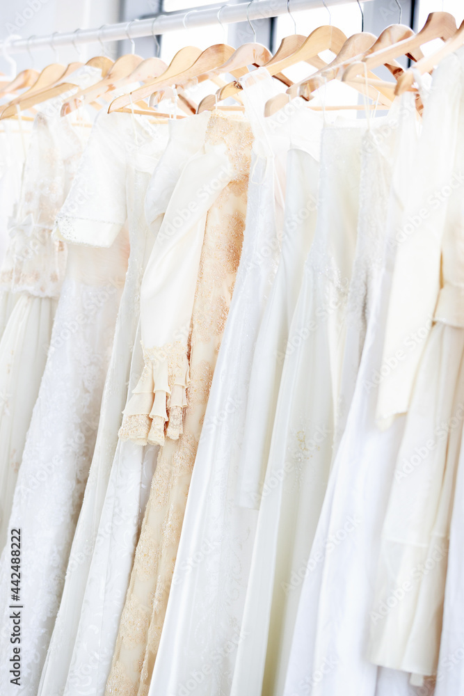 Fototapeta premium Assortment of dresses hanging on a hanger on the background studio. Many beautiful wedding dresses hang in the store. Concept Luxury bridal gowns shop.