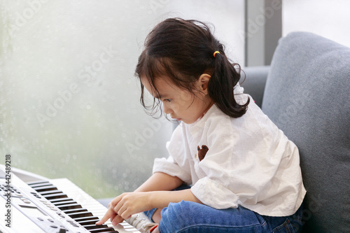 Asian happy girl is playing the piano in a music practice room, the atmosphere outside is raining. Water droplets on the glass. Concept lovely learning education.