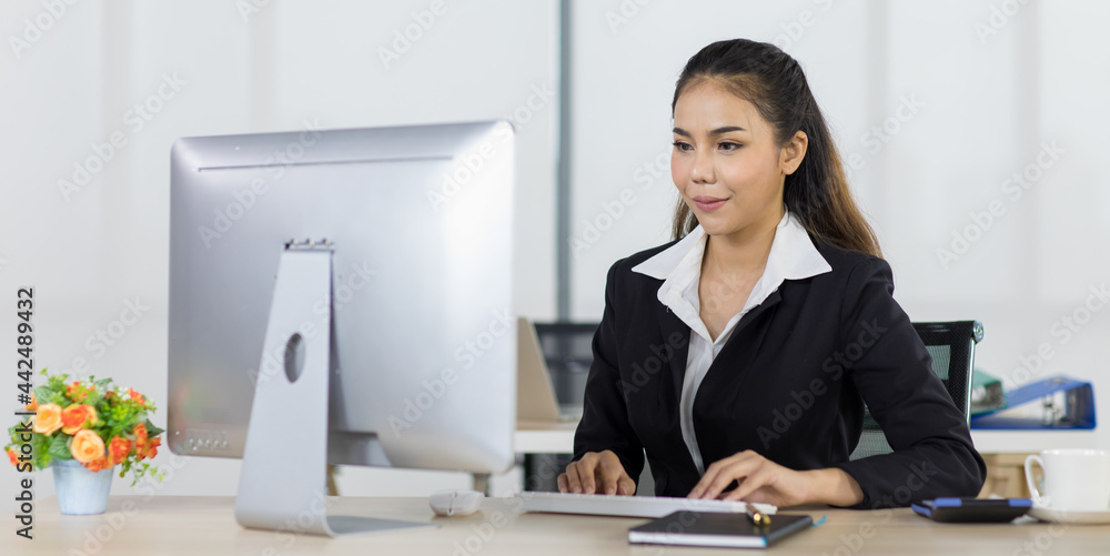 Focus to asian woman office people wearing suit sitting at working desk and using computer while smile with happy Focus to asian woman office people wearing suit sitting at working desk and using computer while smile with happy