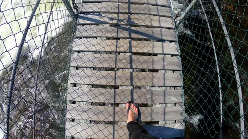 Woman walking in slow motion on a suspension bridge over a rippling raging river. Point of view, looking down. Mårdseleforesen, North of Sweden. Summertime.  photo