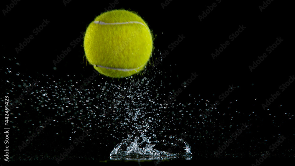 Freeze motion of falling tennis ball on water surface, black background.