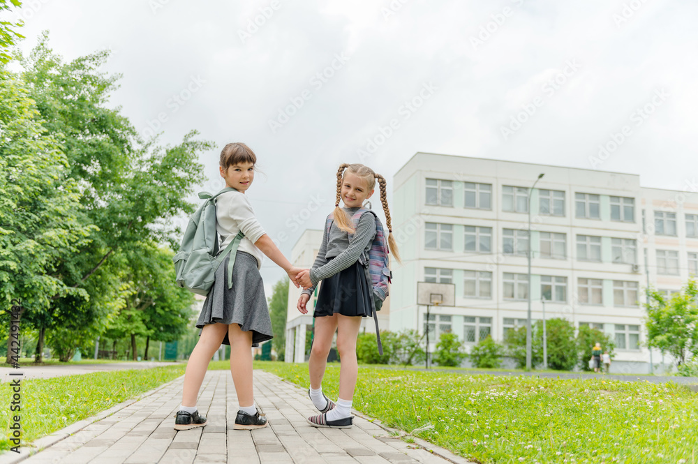 two cute happy girls schoolgirls with backpacks are playing near the school. High quality photo