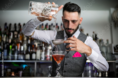 Bartender with sieve pouring drink into glass