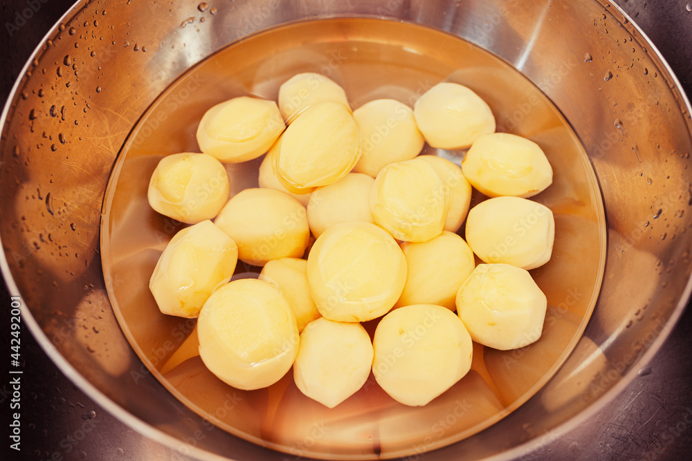 Raw, peeled potatoes submerged in water in chrome bowl in the sink Raw, peeled potatoes submerged in water in chrome bowl in the sink