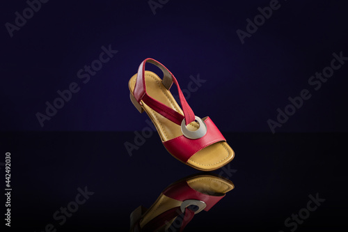 Single red leather women’s sandal on dark blue background. Product photography and shopping concept