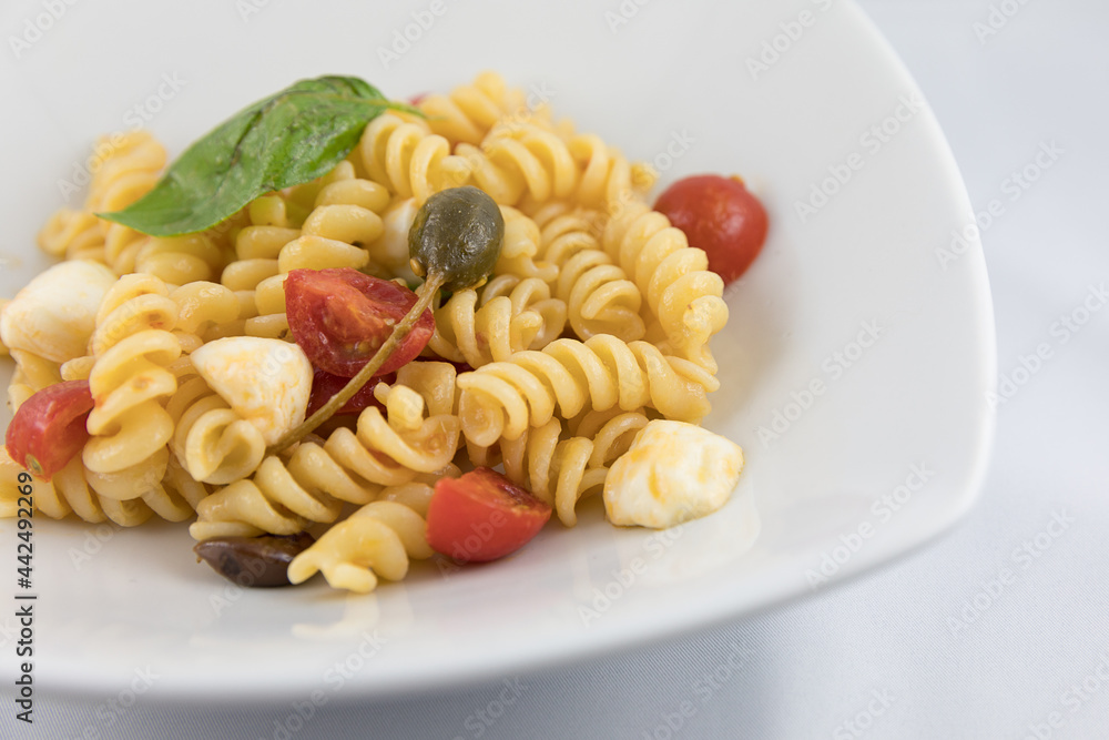 Piatto di pasta con pomodori, mozzarella, olive, capperi e basilico su sfondo bianco Piatto di pasta con pomodori, mozzarella, olive, capperi e basilico su sfondo bianco