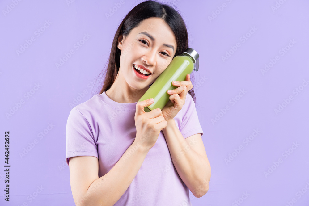 Young Asian woman holding a bottle of juice on purple background Young Asian woman holding a bottle of juice on purple background