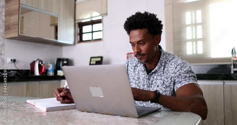 Focused African man using laptop computer at home kitchen table Focused African man using laptop computer at home kitchen table