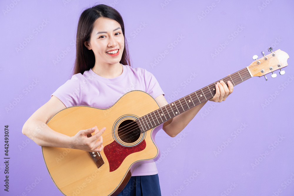 Young Asian woman playing guitar on purple background Young Asian woman playing guitar on purple background
