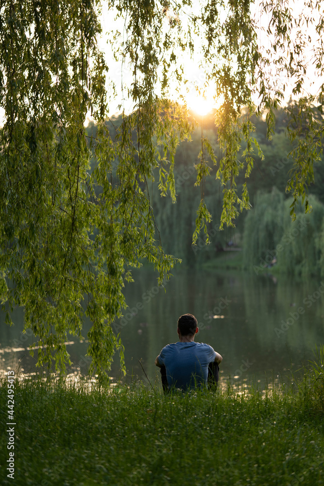 Fototapeta premium young guy alone with thoughts on the lake. Concept: sunset, tranquility