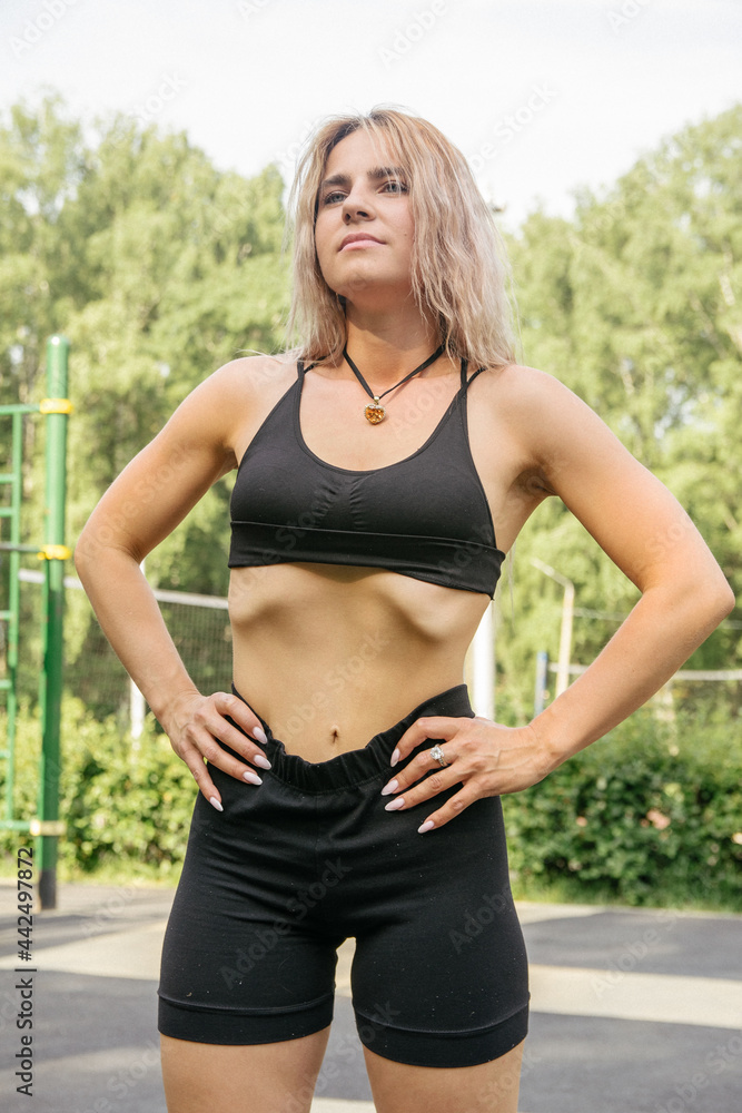 A blonde girl in a sports uniform: black shorts and a black crop-top performs a vacuum of the abdomen A blonde girl in a sports uniform: black shorts and a black crop-top performs a vacuum of the abdomen