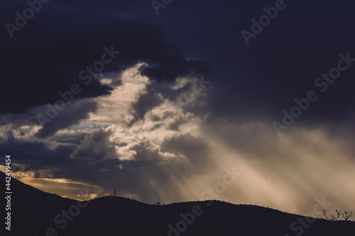 thick stormy clouds over the mountains with intense sun rays peaking through and contrasty light