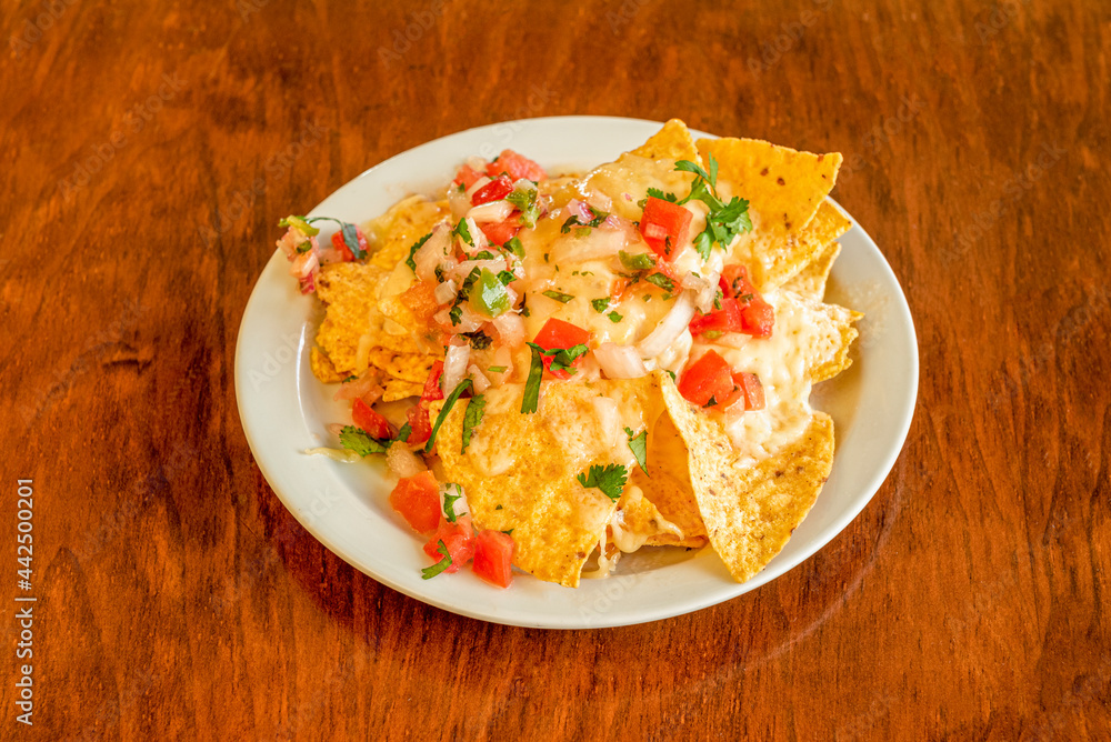 Corn nachos with pico de gallo, parsley and coriander and melted cheese on white plate and wooden table