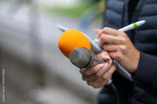 News reporter or TV journalist at press conference, holding microphone and writing notes photo