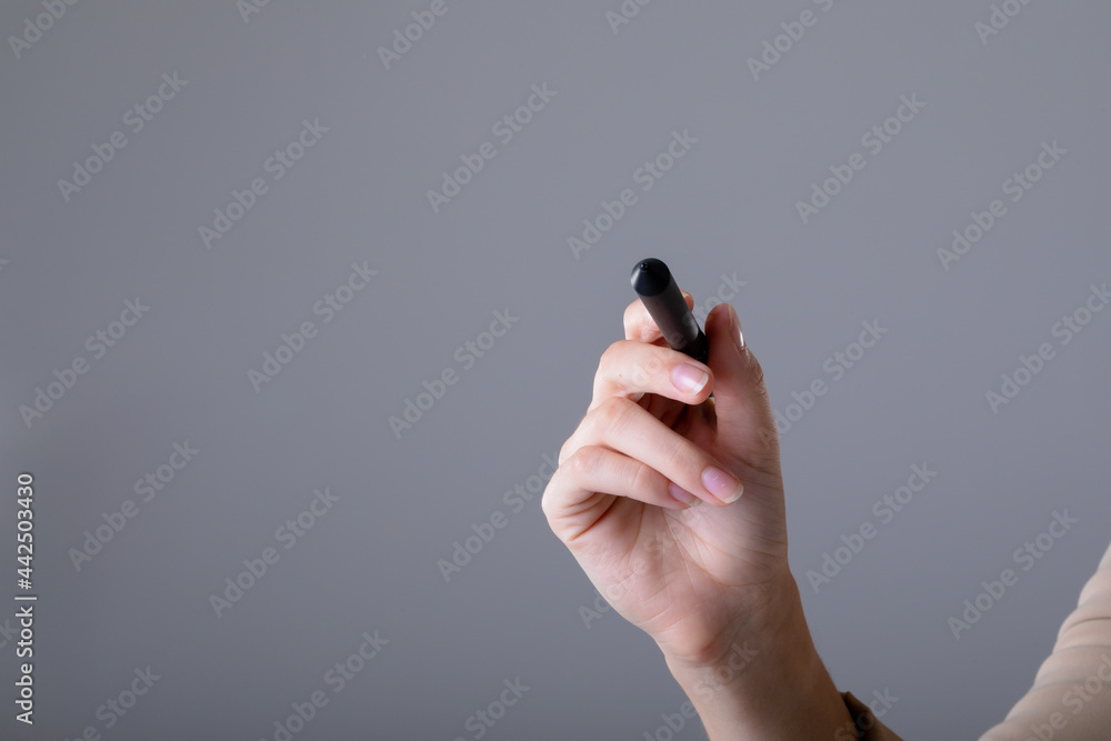 Midsection of caucasian businesswoman holding pen, isolated on grey background