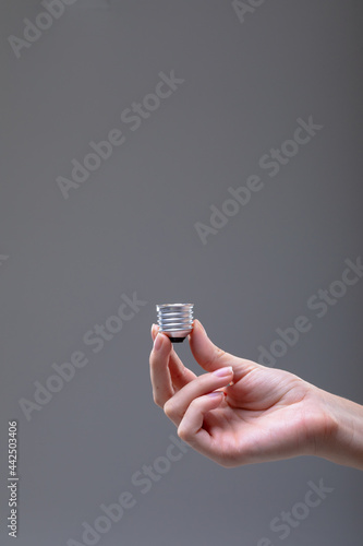 Close up of caucasian businesswoman holding base of light bulb, isolated on grey background