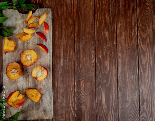 top view of halves of fresh ripe peaches on a wooden cutting board with green leaves on rustic background with copy space