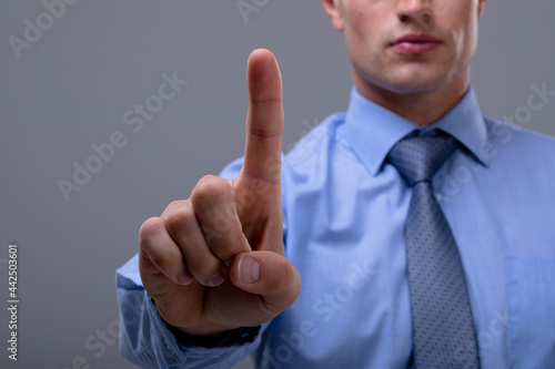 Midsection of caucasian businessman touching virtual interface, isolated on grey background