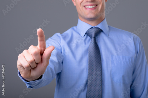 Midsection of caucasian businessman touching virtual interface, isolated on grey background