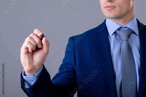 Midsection of caucasian businessman holding pen, isolated on grey background
