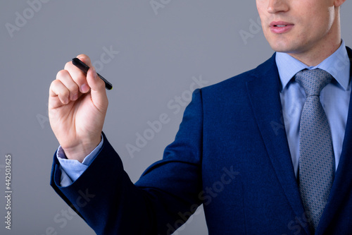 Midsection of caucasian businessman holding pen, isolated on grey background