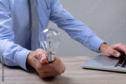 Midsection of caucasian businessman holding light bulb using laptop, isolated on grey background