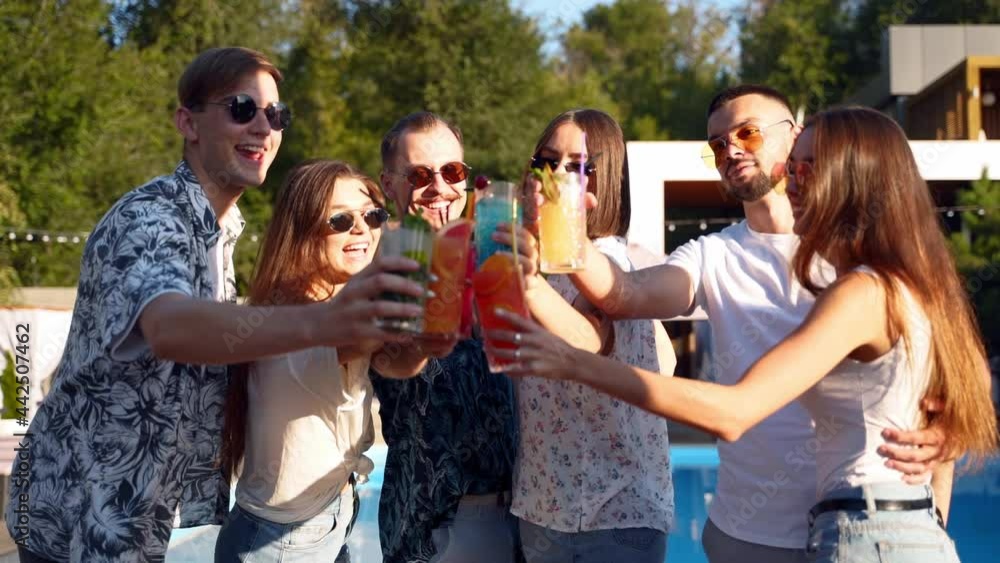 Group of friends having fun at poolside summer party clinking glasses with summer cocktails at camera swimming pool in slow motion. People toast drinking fresh juice. Luxury villa on tropical vacation Group of friends having fun at poolside summer party clinking glasses with summer cocktails at camera swimming pool in slow motion. People toast drinking fresh juice. Luxury villa on tropical vacation