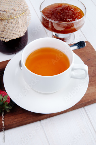 side view of a cup of tea with strawberry jam in a glass vase on wooden board on white background