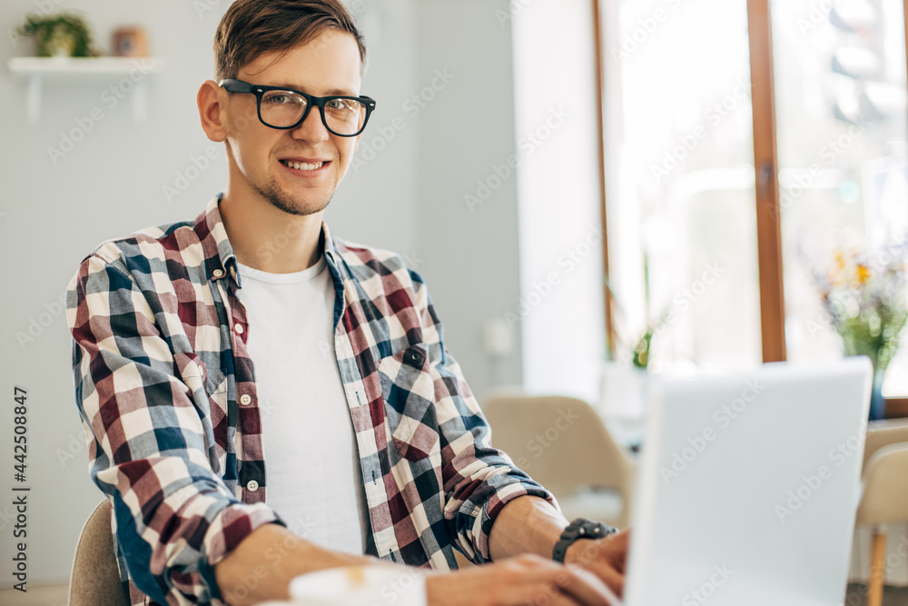 young man wearing glasses, uses laptop for video call on laptop computer, sits in a cafe and drinks a cup of coffee young man wearing glasses, uses laptop for video call on laptop computer, sits in a cafe and drinks a cup of coffee