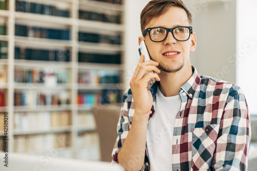 business man with laptop talking on mobile phone in office against background with library